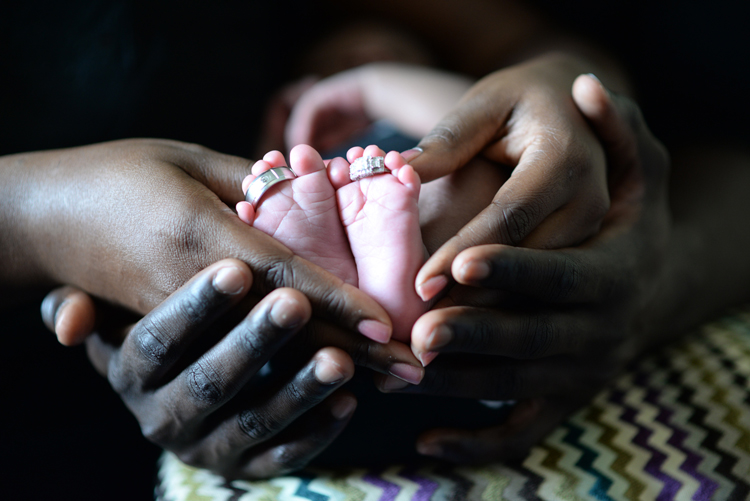le mani intrecciate dei due genitori accolgono i piccoli piedi del loro bimbo