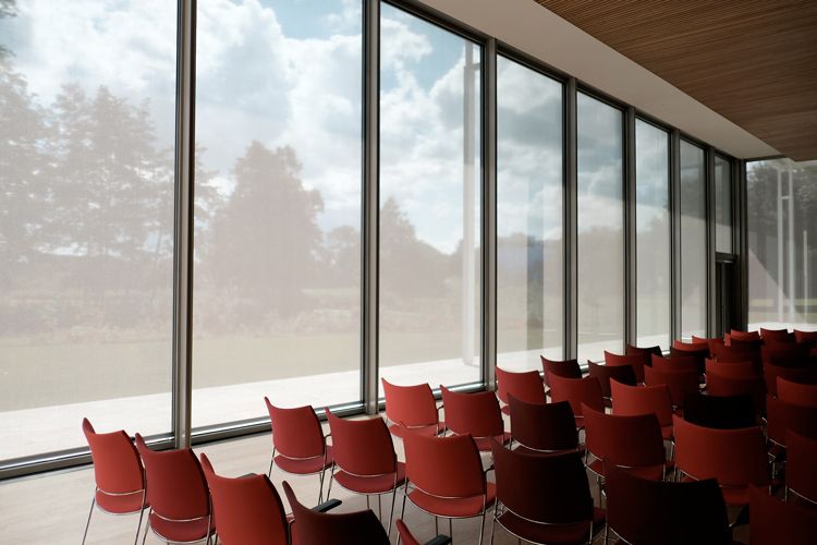 adisco apuania odv convocazione assemmblea ordinaria 2020: 
scorcio da interno verso esterno di una sala riunioni con sedie rosse e parete laterale sinistra in vetro fotografata dalla parete posteriore